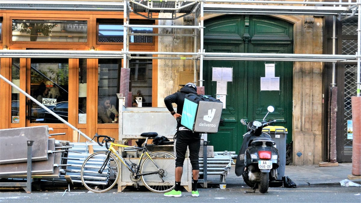 Delivery rider outside a Paris restaurant, stood next to his bike adjusting the bag on his back. Photo by Carl Campbell on ht