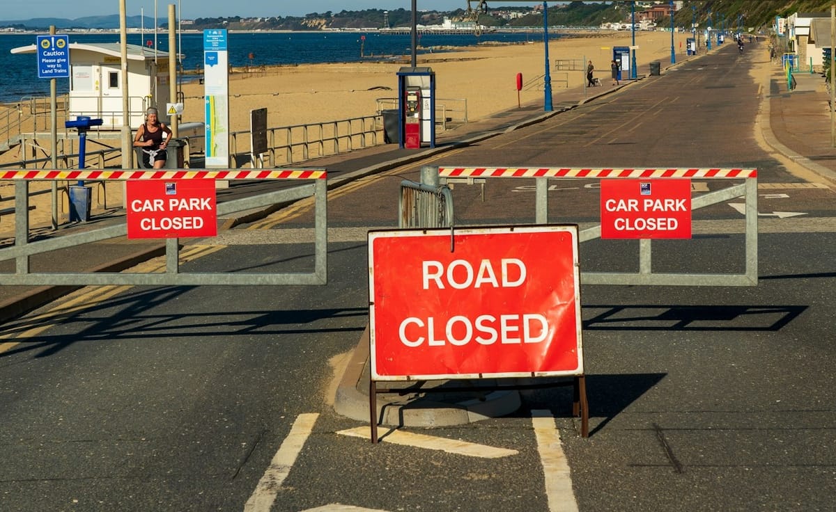 Road closed sign and barriers blocking the road down to a sandy beach